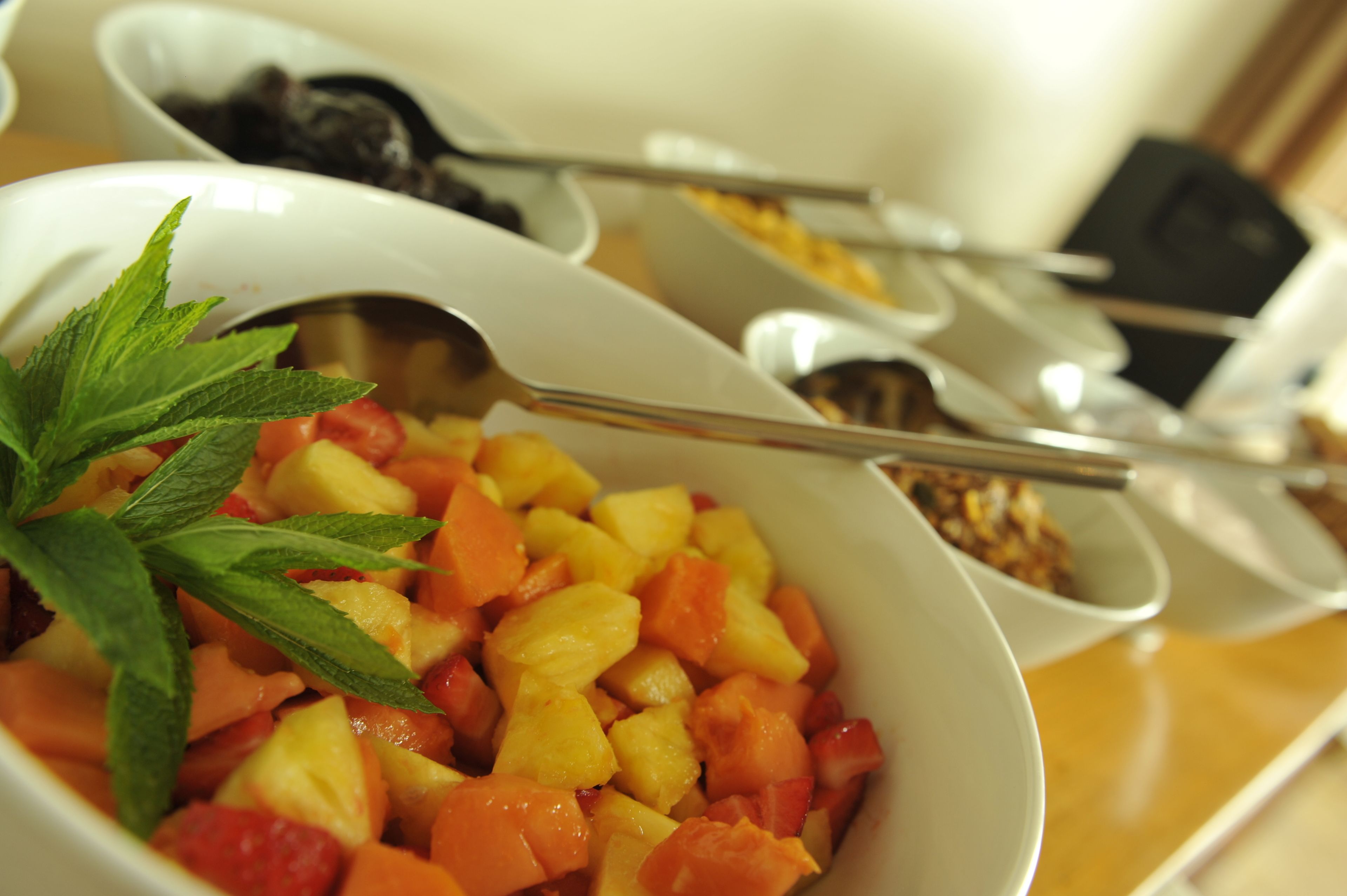 Eine Schüssel Obstsalat mit Minze, ein Löffel und ein Becher Granola.