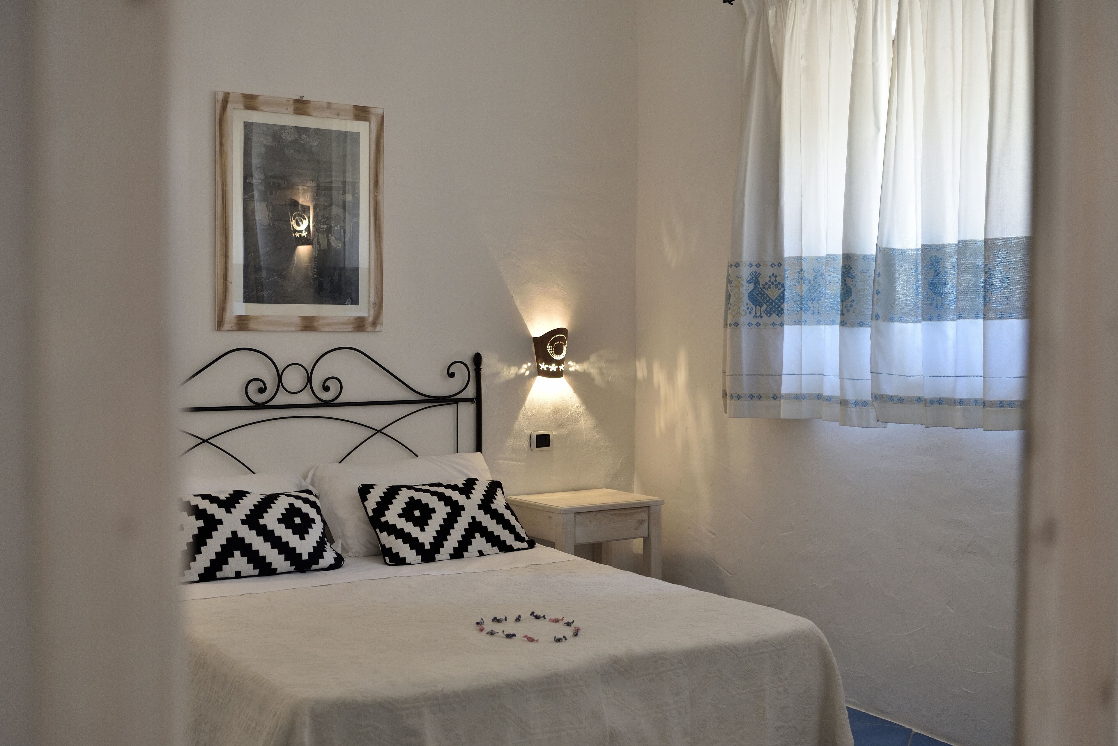 Een net opgemaakt bed met gestreepte kussens, een nachtkastje met een lamp en een ingelijste foto aan de muur.