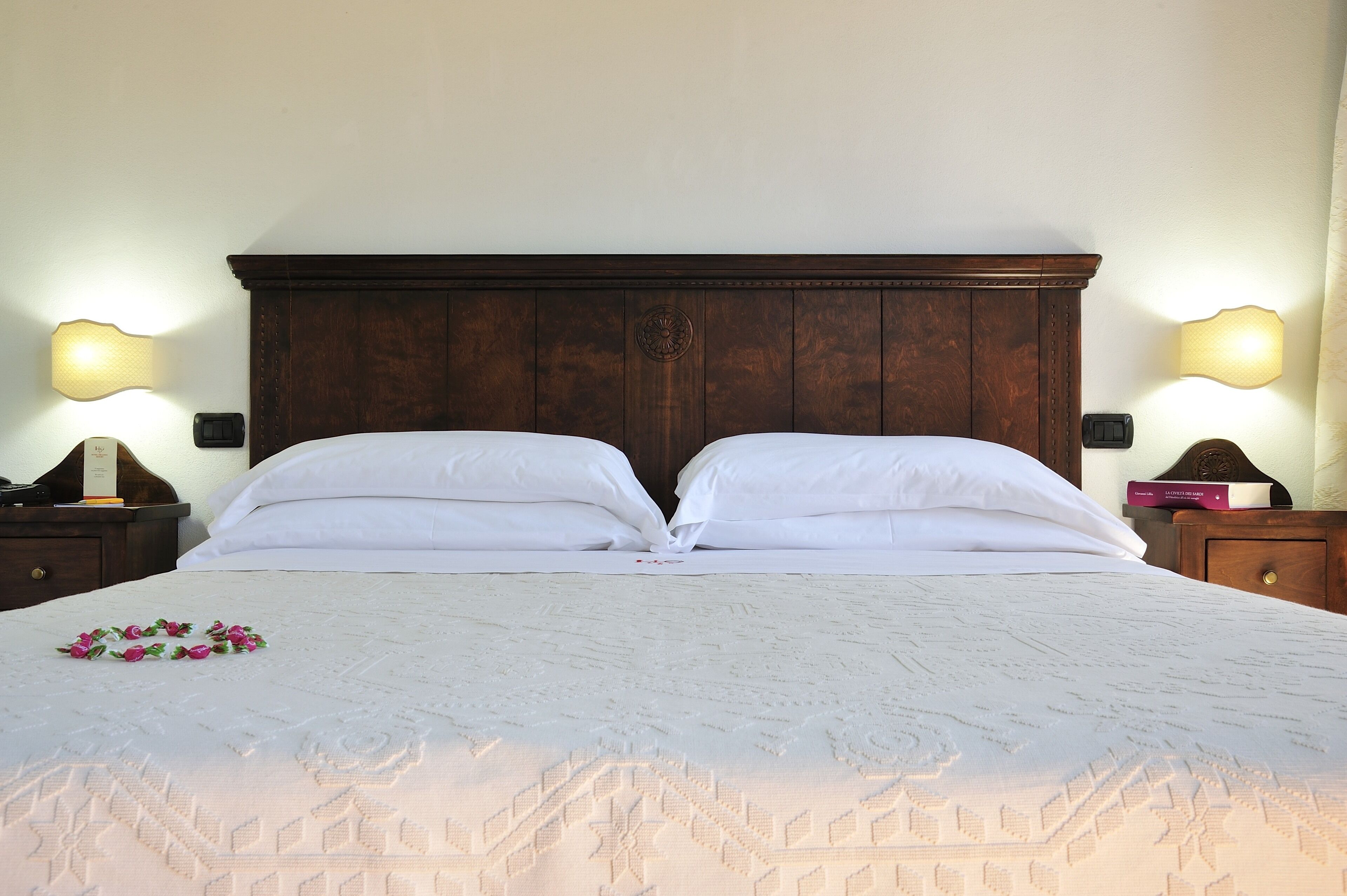 A neatly made bed with white linens and a decorative headboard.