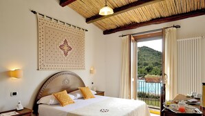 A hotel room with a large bed, a wooden headboard, a wall hanging, and a balcony with a view of a mountain and a pool.
