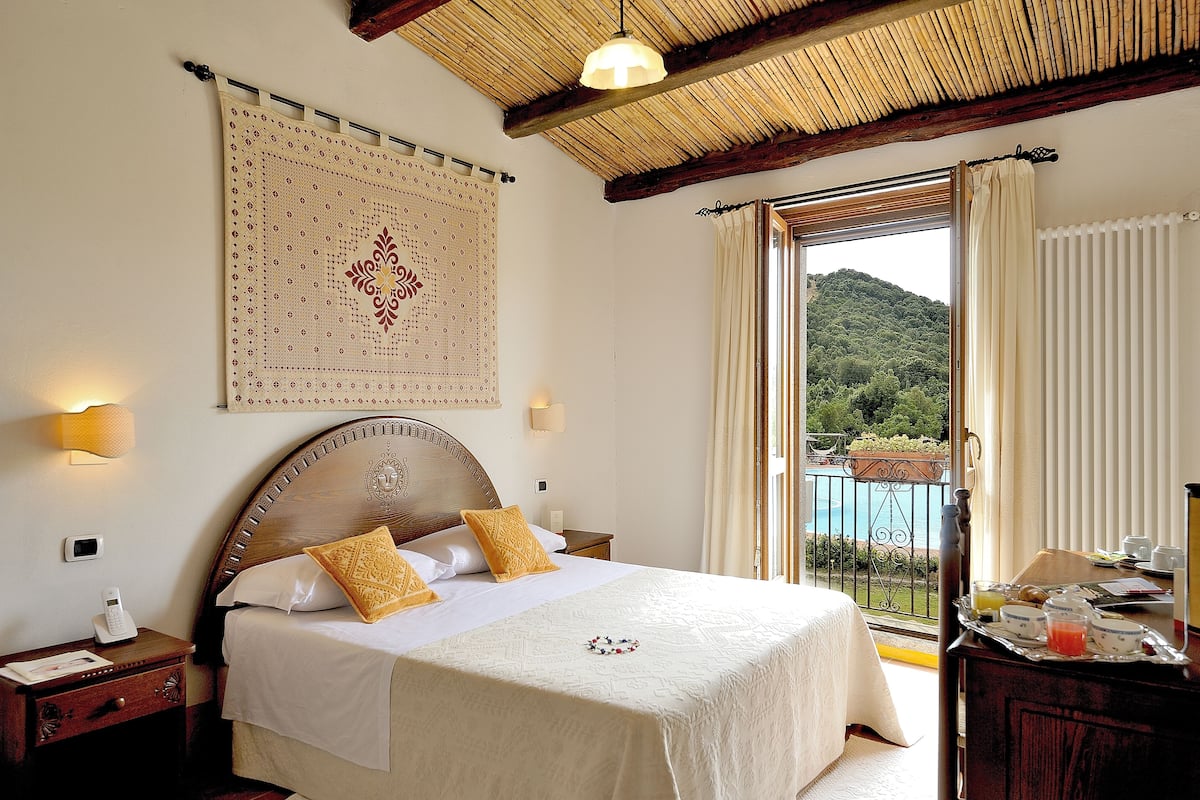 Ein Hotelzimmer mit einem großen Bett, einem Holzkopfstück, einer Wanddekoration und einem Balkon mit Blick auf einen Berg und einen Pool.