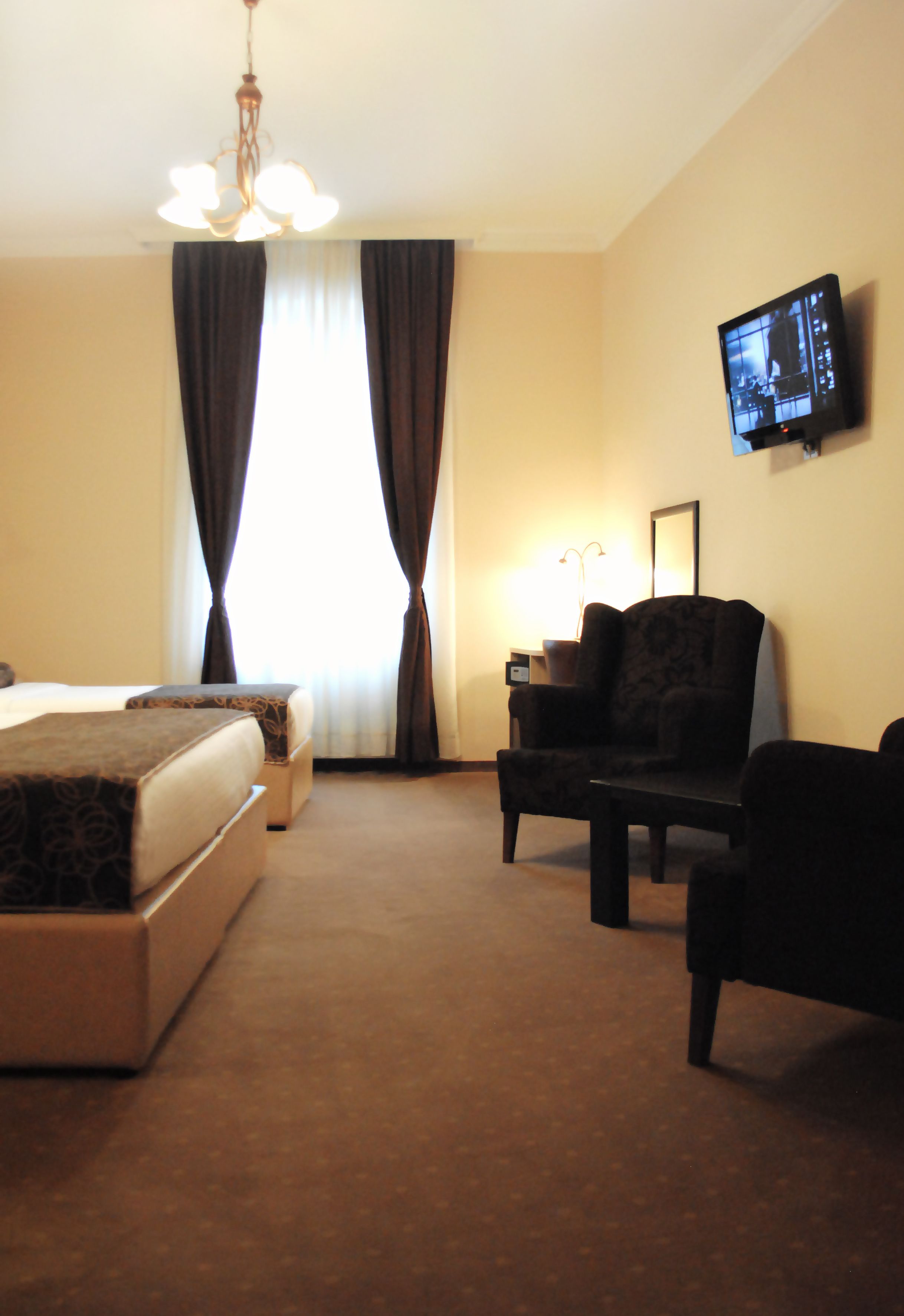 Ein Hotelzimmer mit Bett, Sessel, Schreibtisch, Fernseher und einem Fenster mit Vorhängen.
