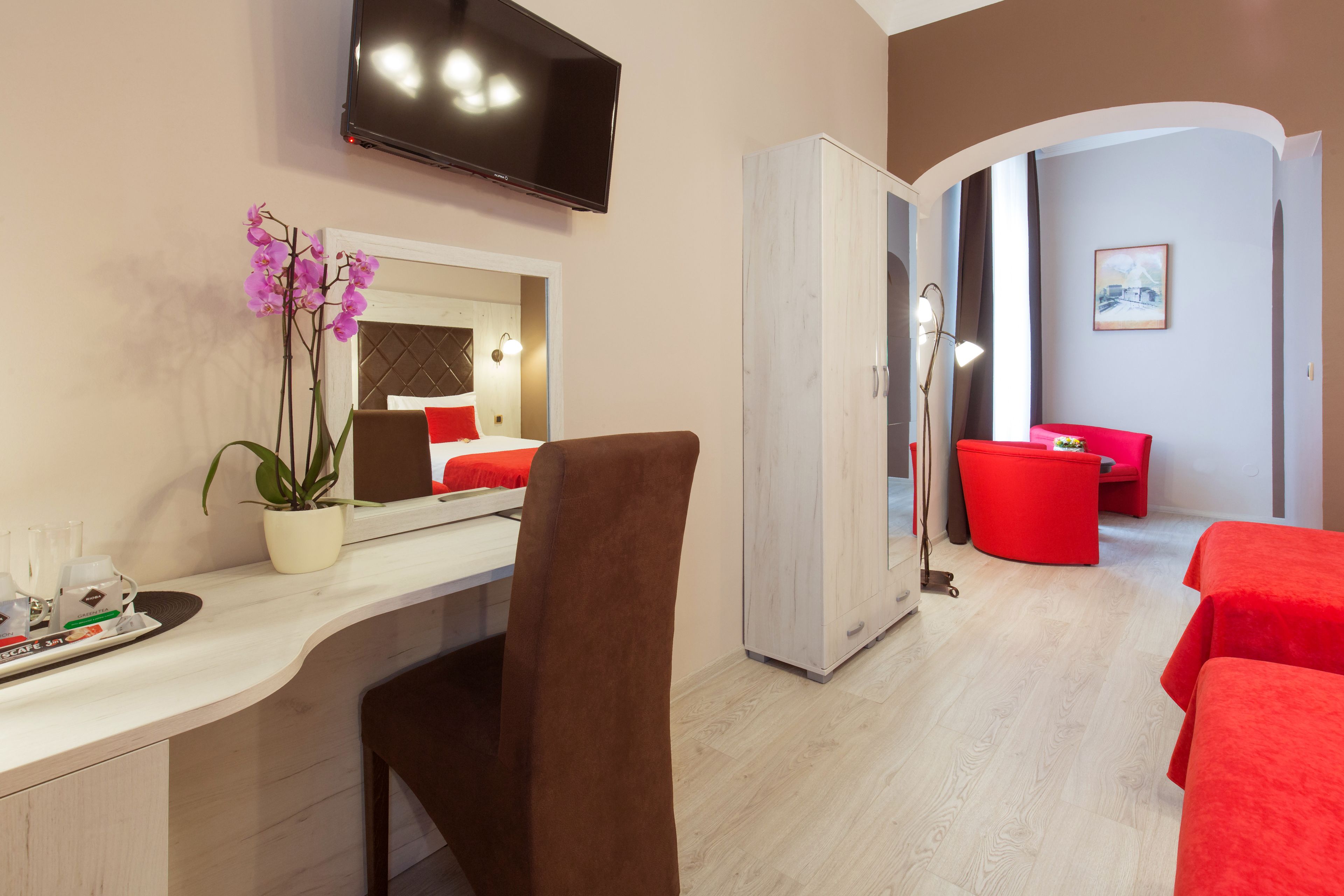A hotel room with a bed, a desk, a TV, a wardrobe, and a red sofa.