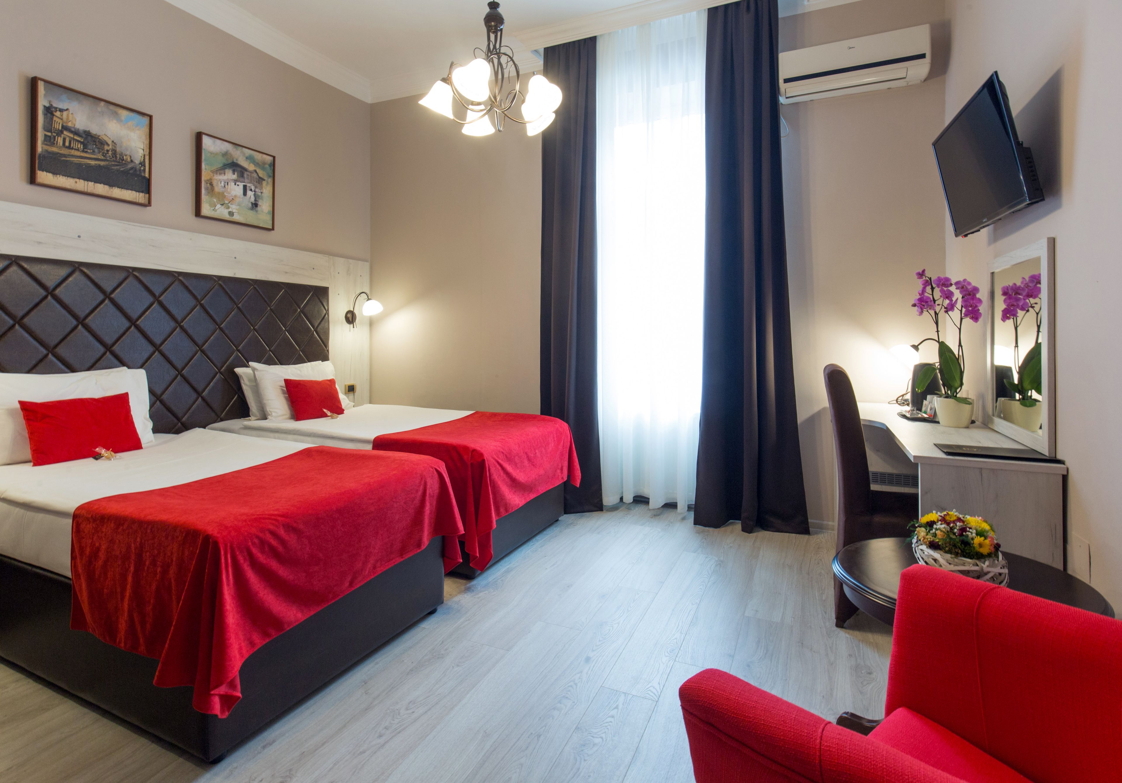 A hotel room with two beds, a desk, a chair, a TV, and a window with curtains.
