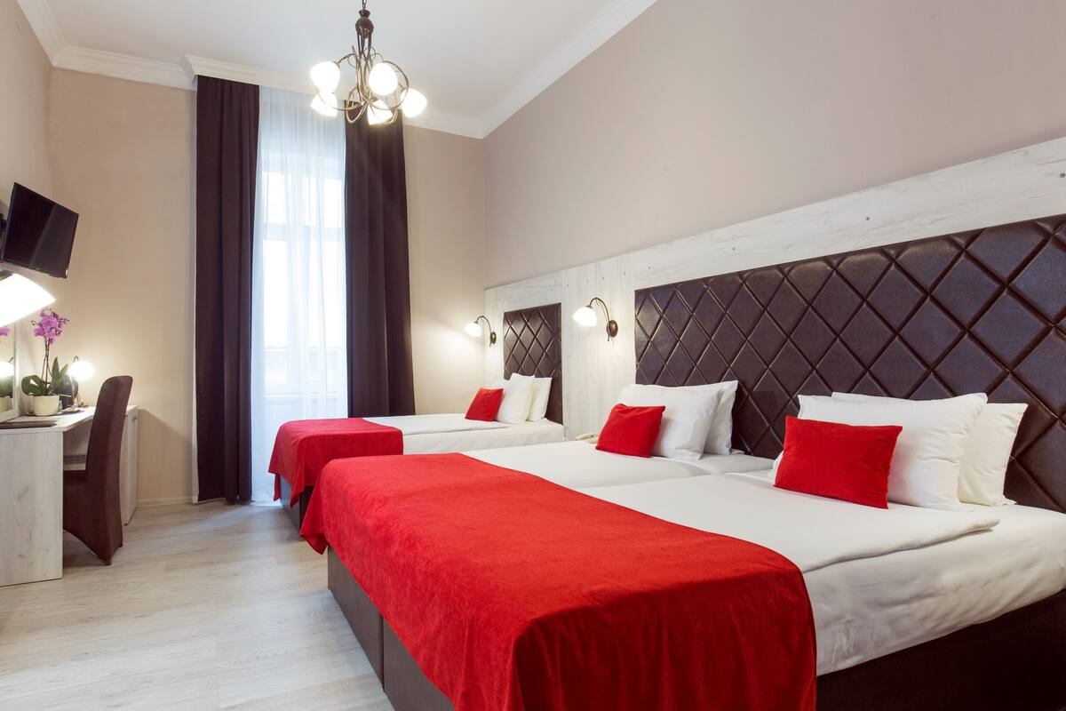Habitación de hotel con tres camas, un escritorio con silla, televisor y ventana con cortinas.