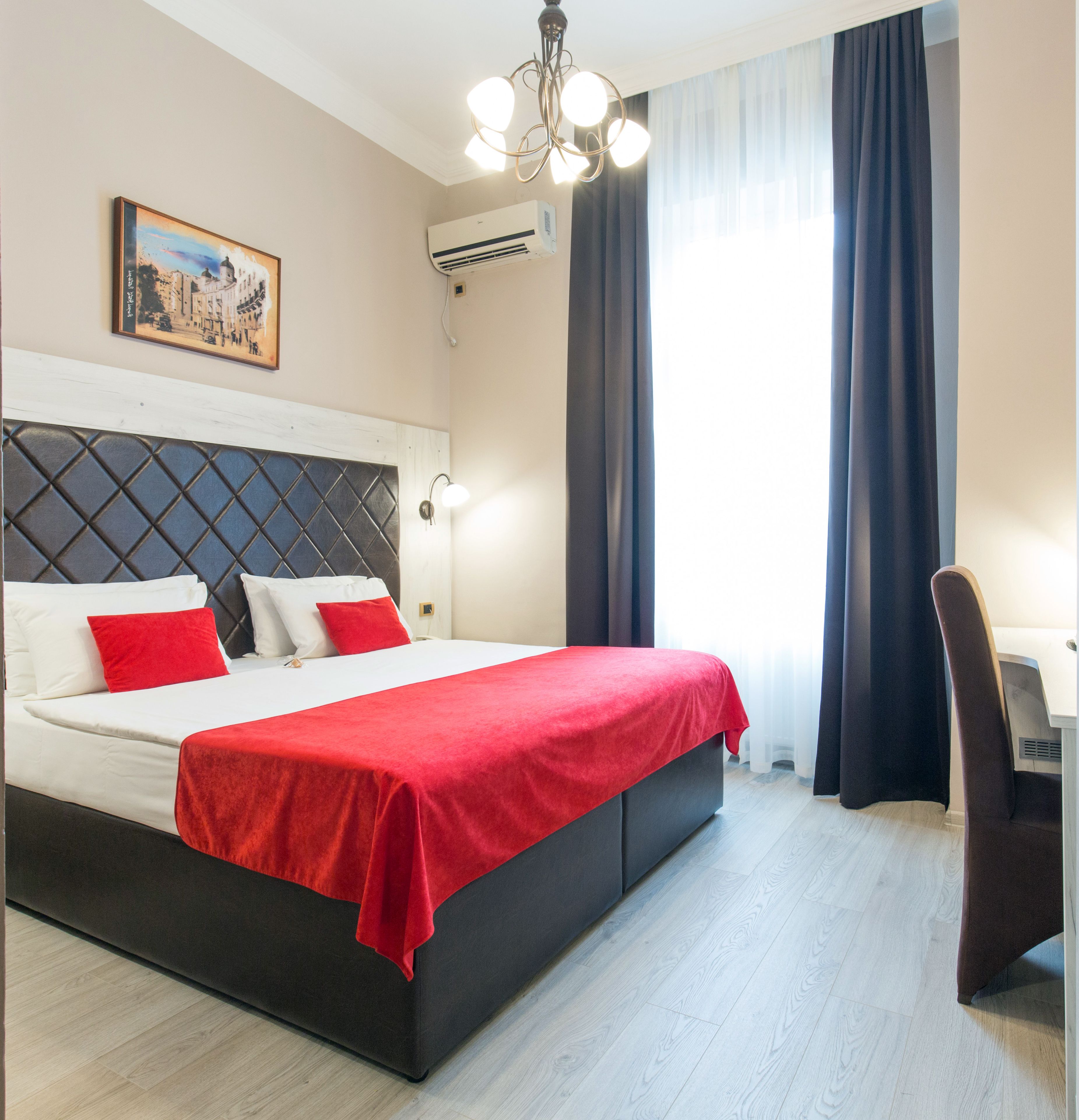 Een hotelkamer met een bed, een bureau, een stoel, een schilderij en een raam met gordijnen.