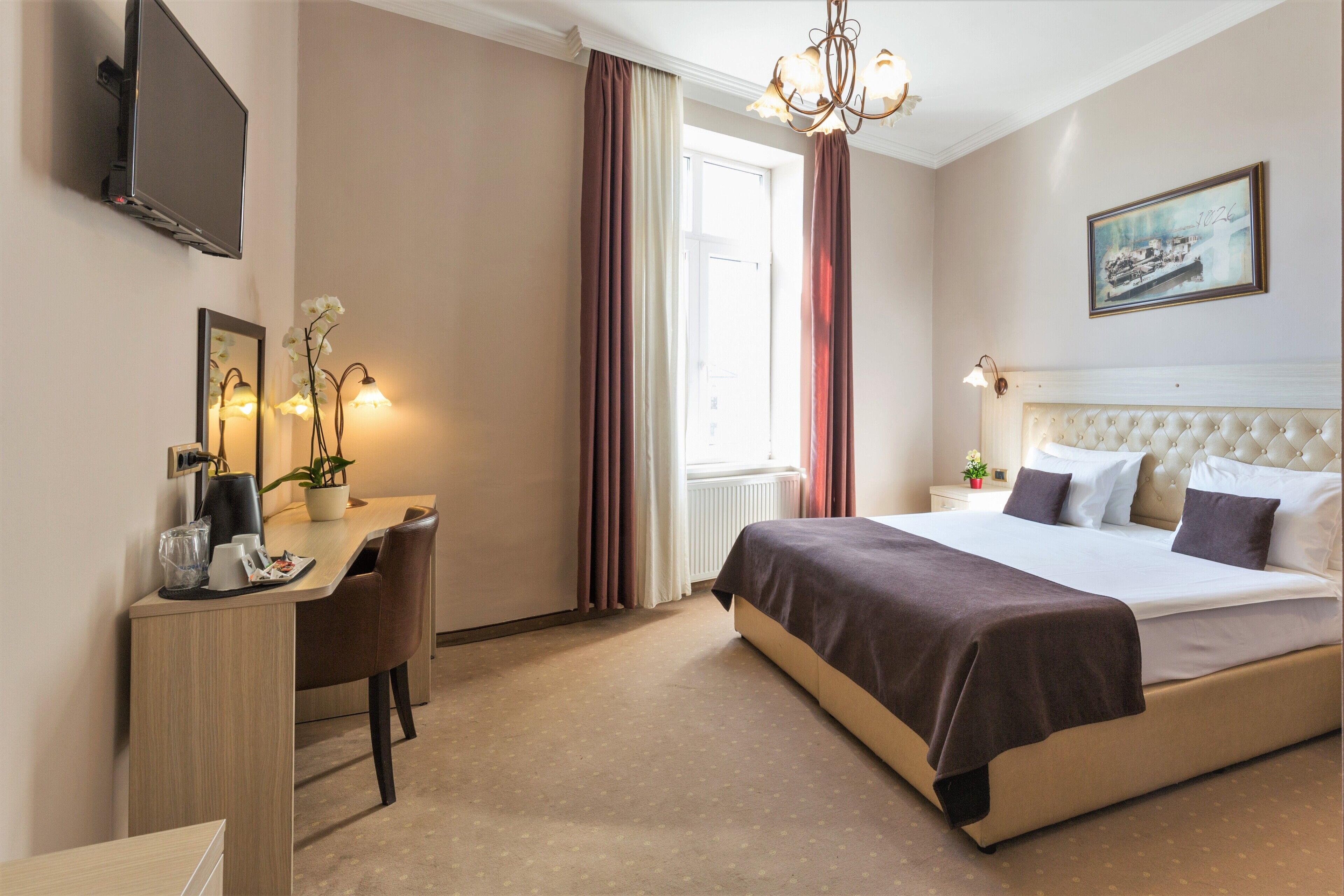 A hotel room with a bed, a desk, a chair, a television, and a window with curtains.