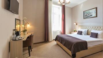 A hotel room with a bed, a desk, a chair, a television, and a window with curtains.