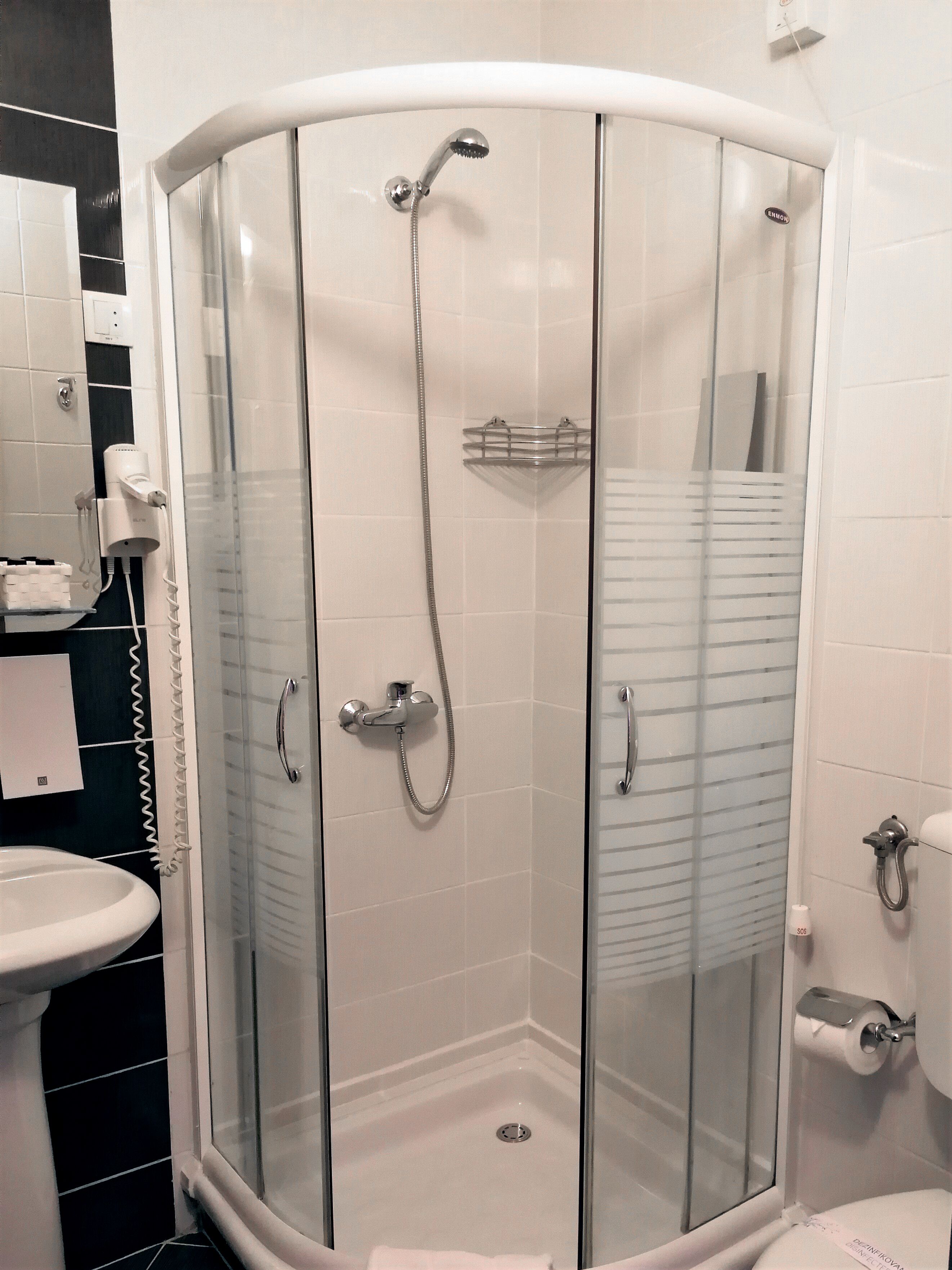 A glass-enclosed shower with a handheld showerhead and a wall-mounted faucet.