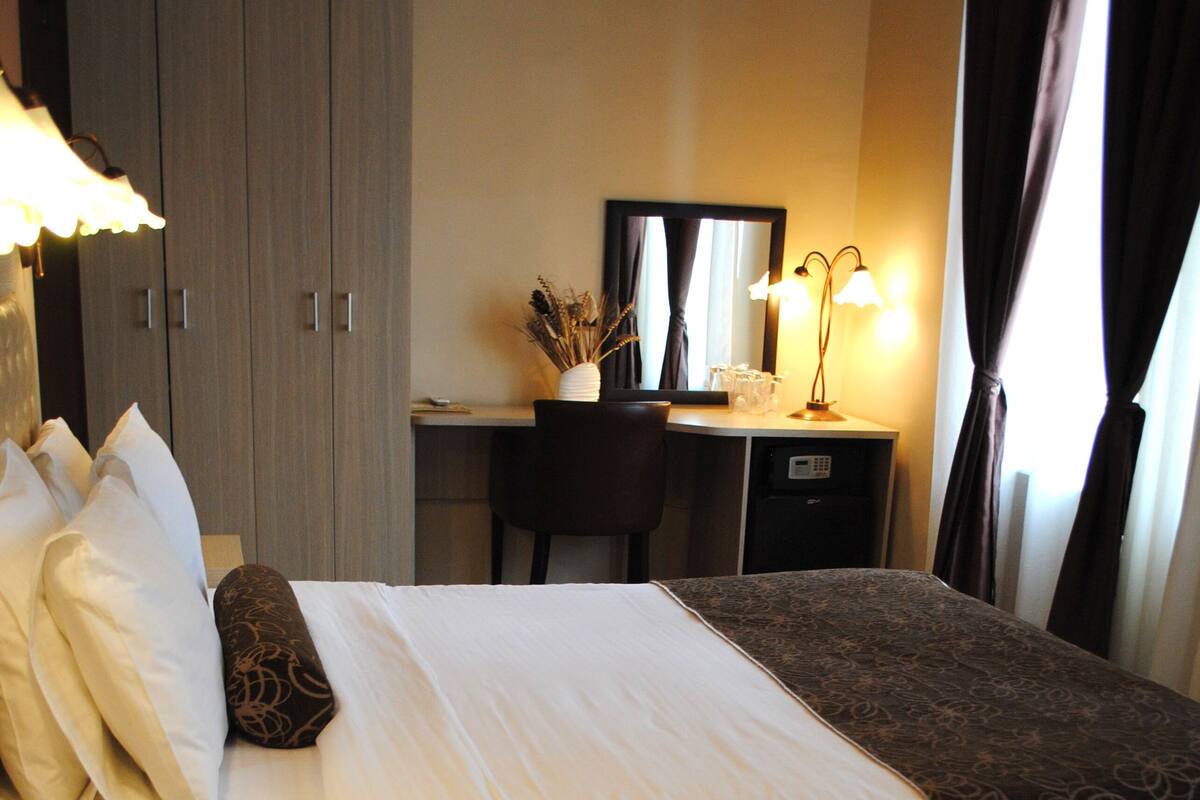 Habitación de hotel con dos camas, un escritorio, una silla, un armario y una lámpara.