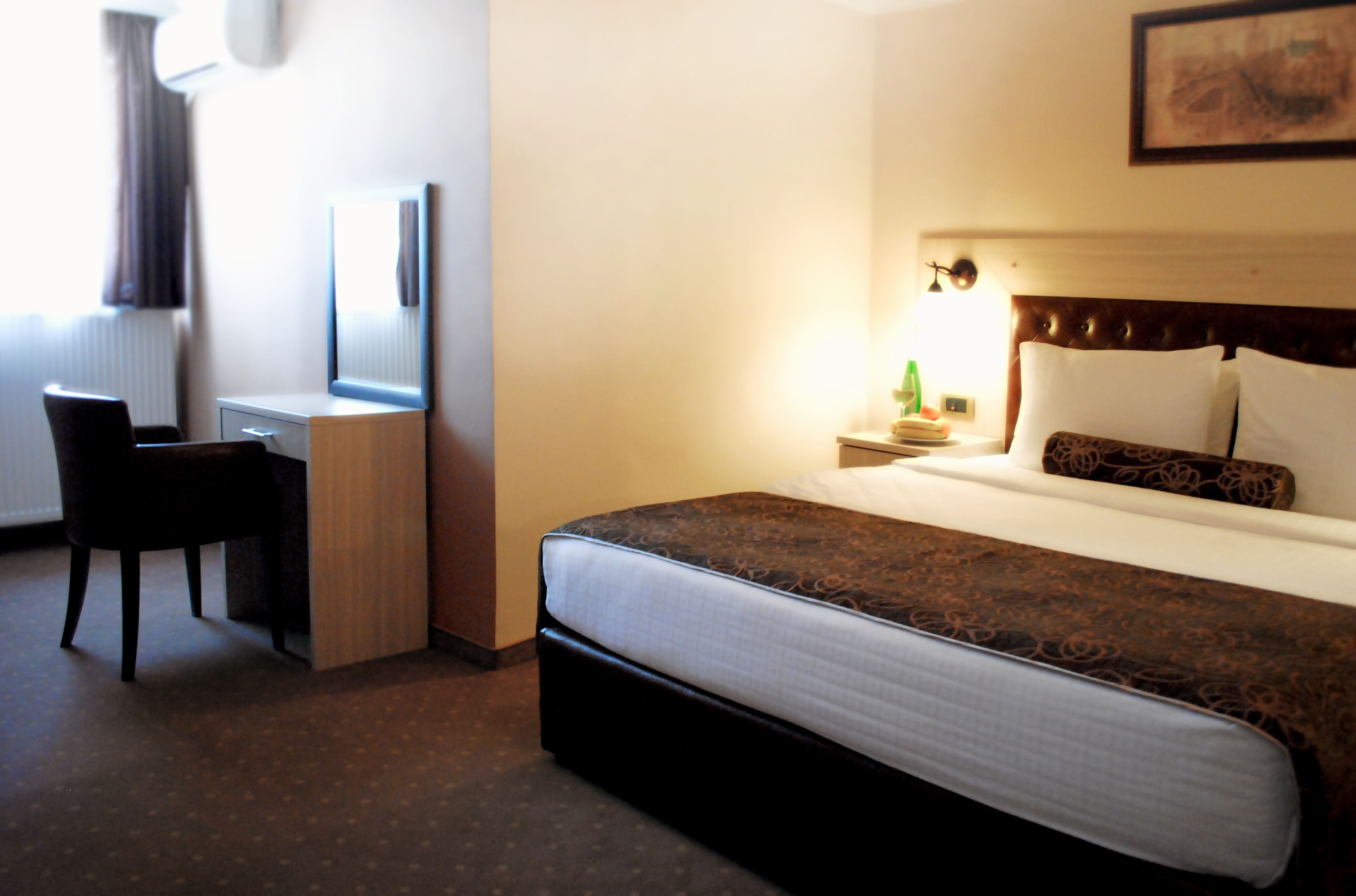 A hotel room with a bed, a desk, a chair, a nightstand, and a lamp.