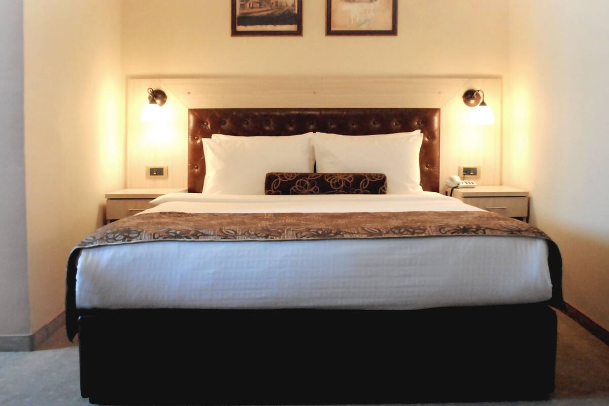 Habitación de hotel con una cama grande, dos mesitas de noche, un cabecero y dos cuadros enmarcados en la pared.