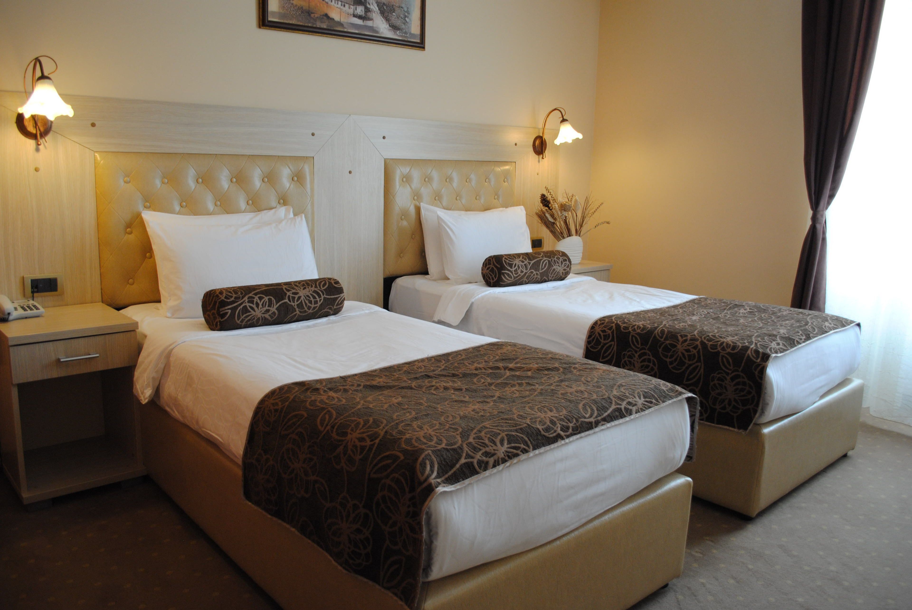 A hotel room with two beds, each with a headboard, bedside tables, and lamps.