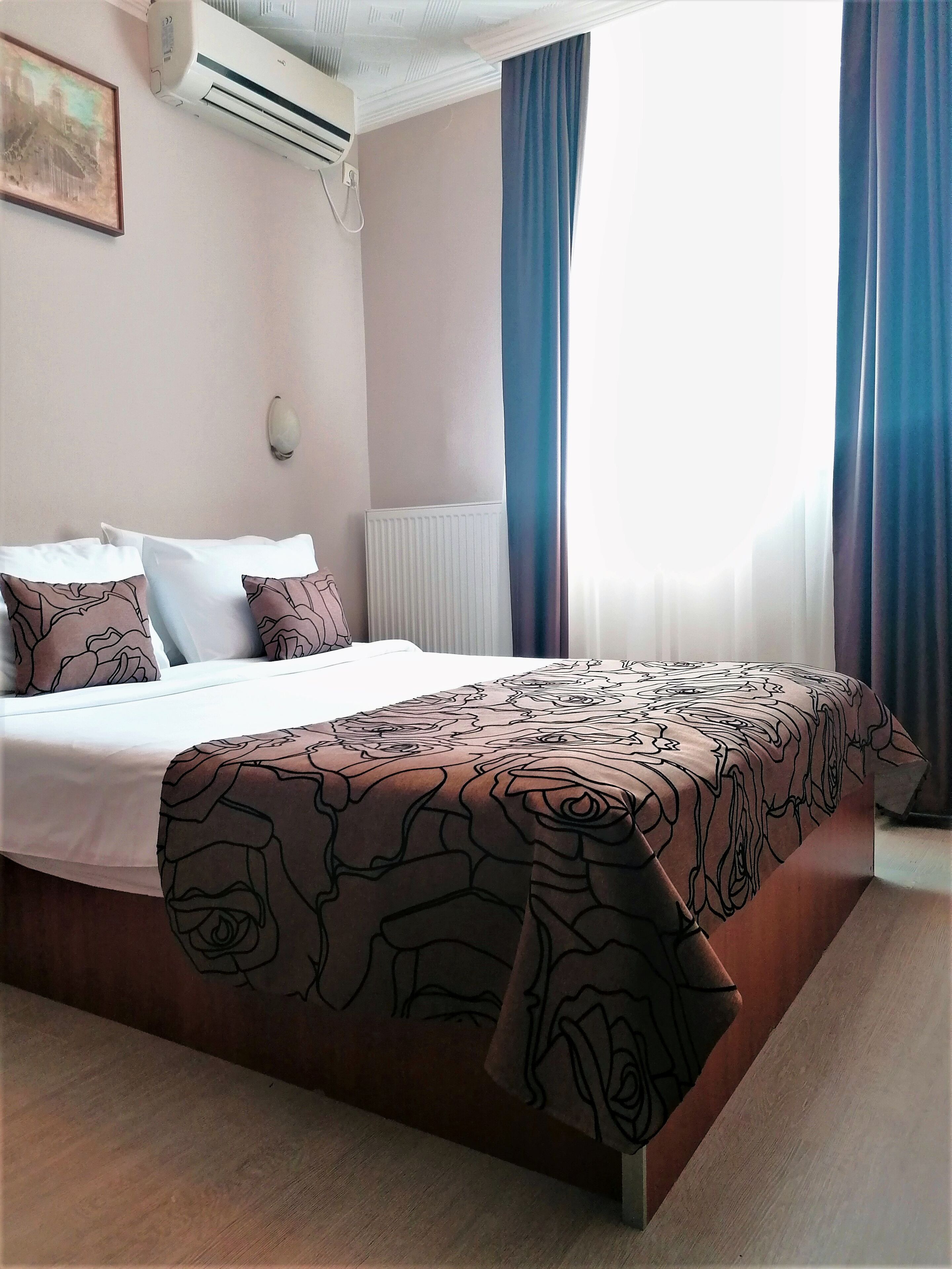 Une chambre d’hôtel équipée d’un lit, d’un appareil de climatisation, d’une fenêtre avec des rideaux et d’une lampe fixée au mur.