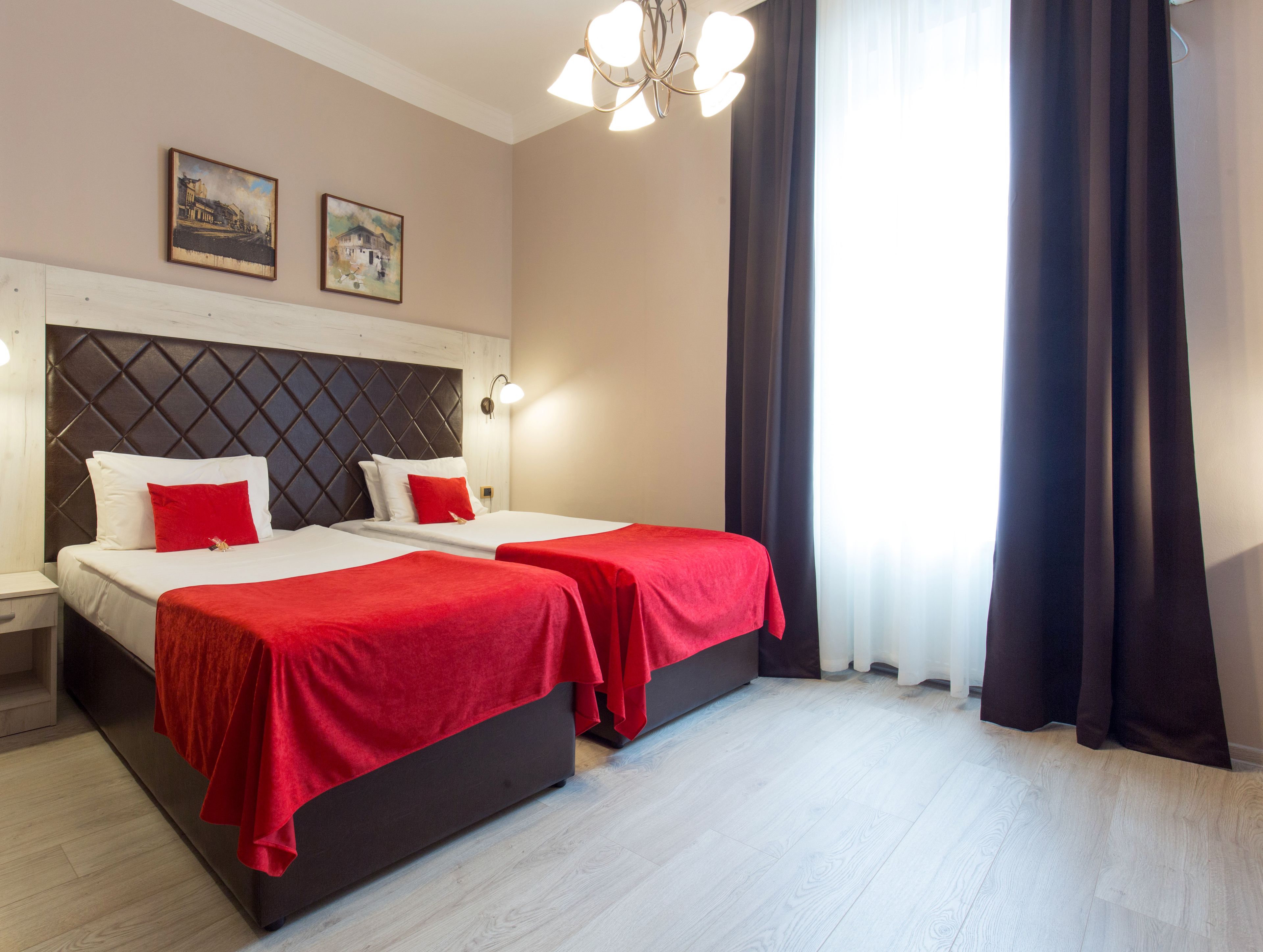 Ein Hotelzimmer mit zwei Betten, einem großen Fenster mit Vorhängen, einer Chandelier und Bildern an der Wand.