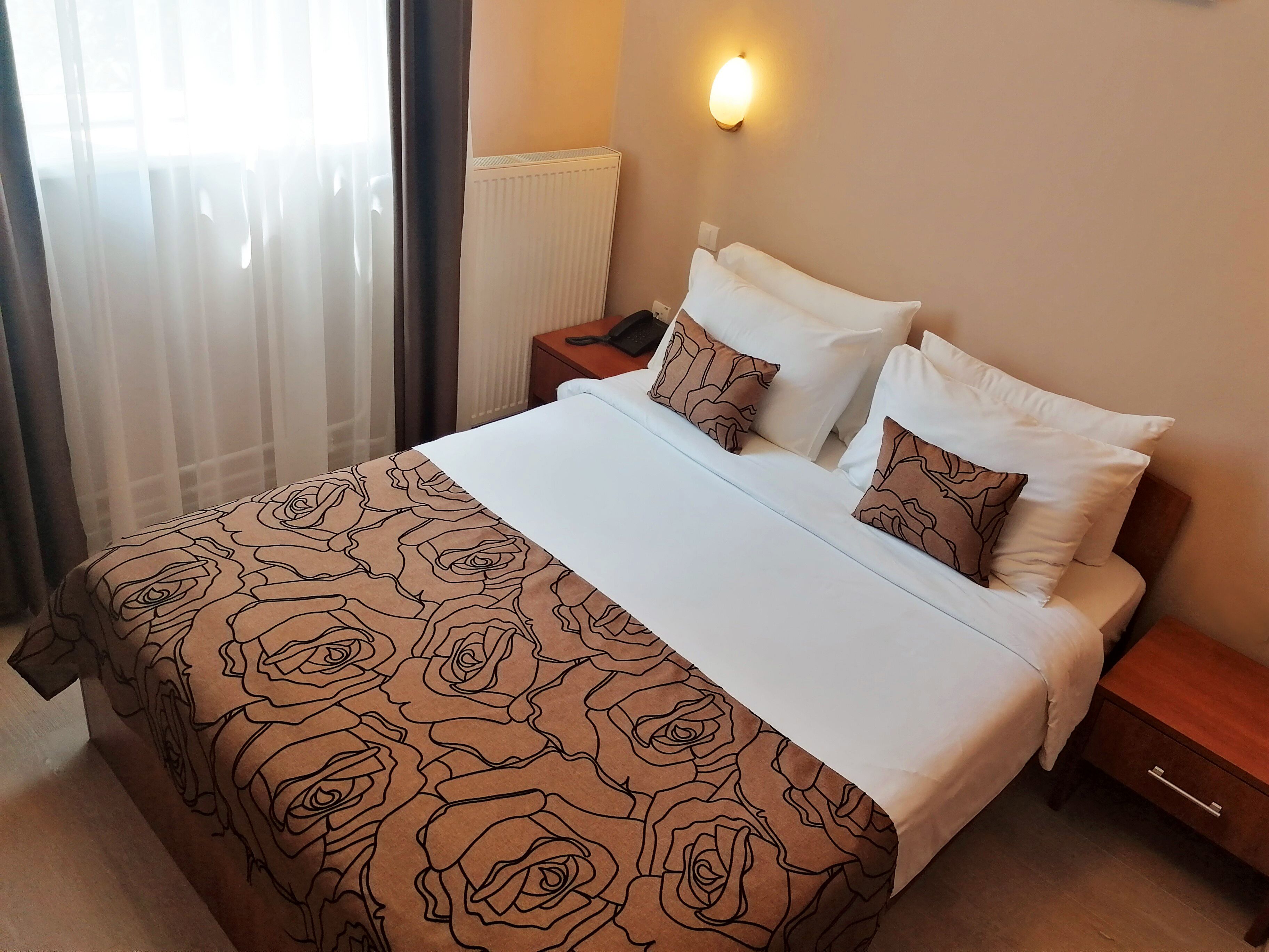 A neatly made bed with a patterned bedspread, a bedside table with a lamp, and a wall-mounted light fixture.