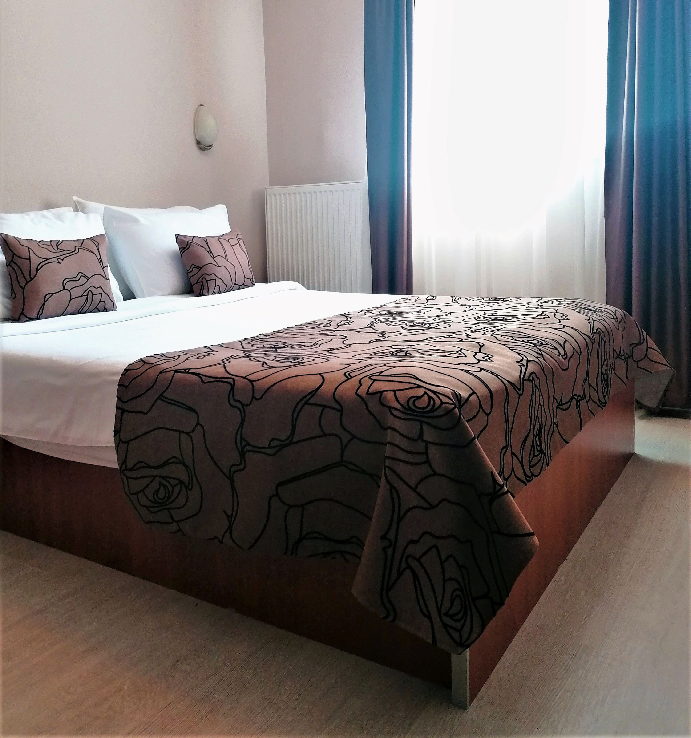 A hotel room with a large bed, a radiator, and a window with curtains.