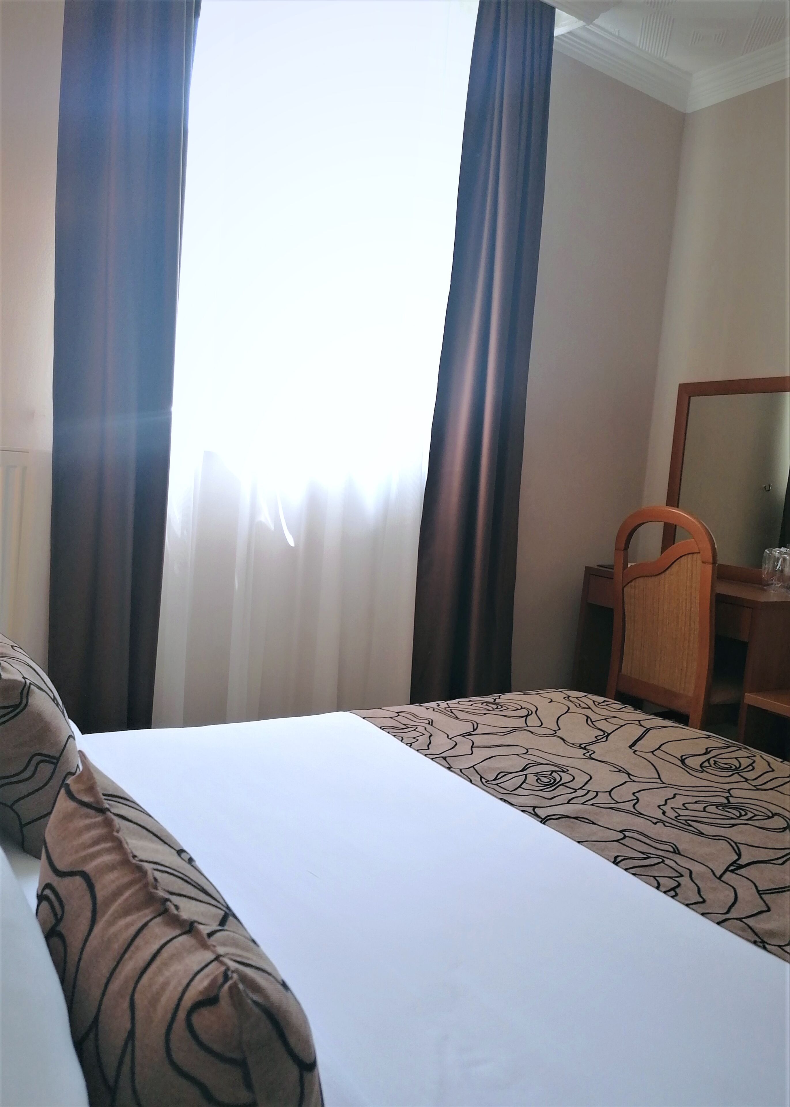 Una habitación de hotel con una cama, una silla de madera, un escritorio y un espejo.