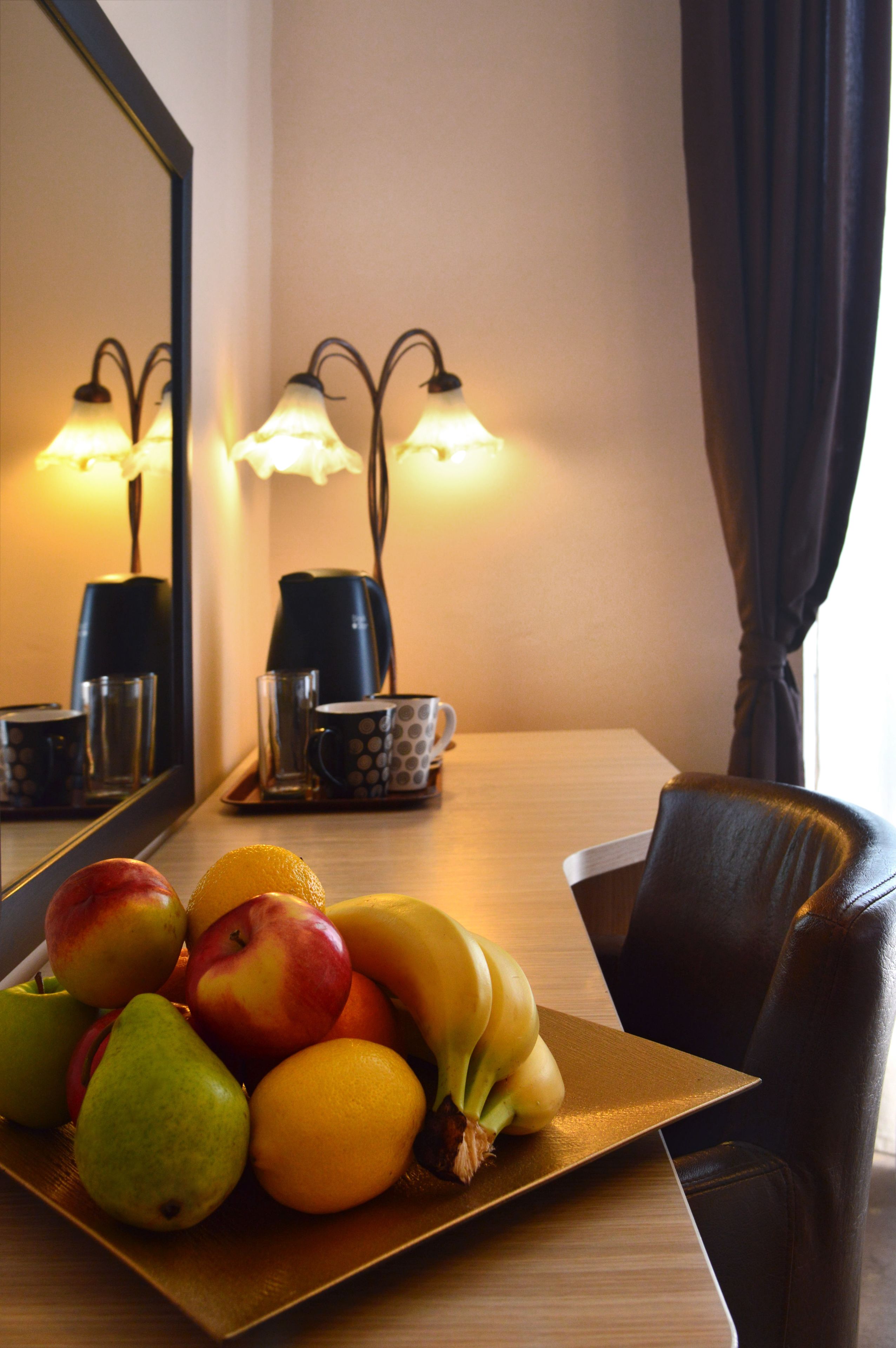 A dining table with a fruit platter, a coffee maker, and a cup of coffee.