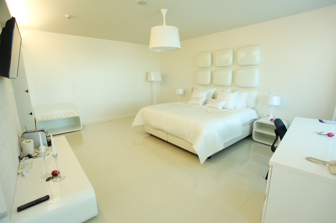 A modern hotel room with a large bed, bedside tables, a desk, and a white color scheme.