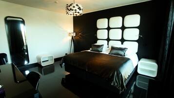 A modern hotel room with a large bed, a desk, and a unique geometric wall design.