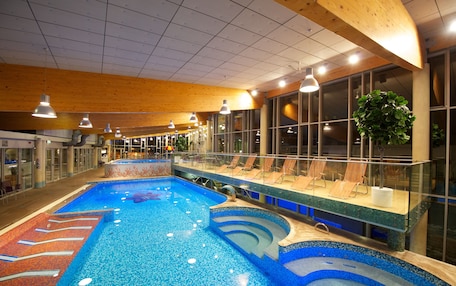 An indoor swimming pool with multiple lanes, lounge chairs, and a large window overlooking the pool area.