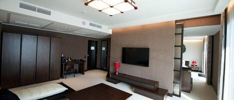 Una moderna camera d'albergo con un letto grande, un divano, un tavolino, una TV fissata al muro e una scrivania con una sedia.
