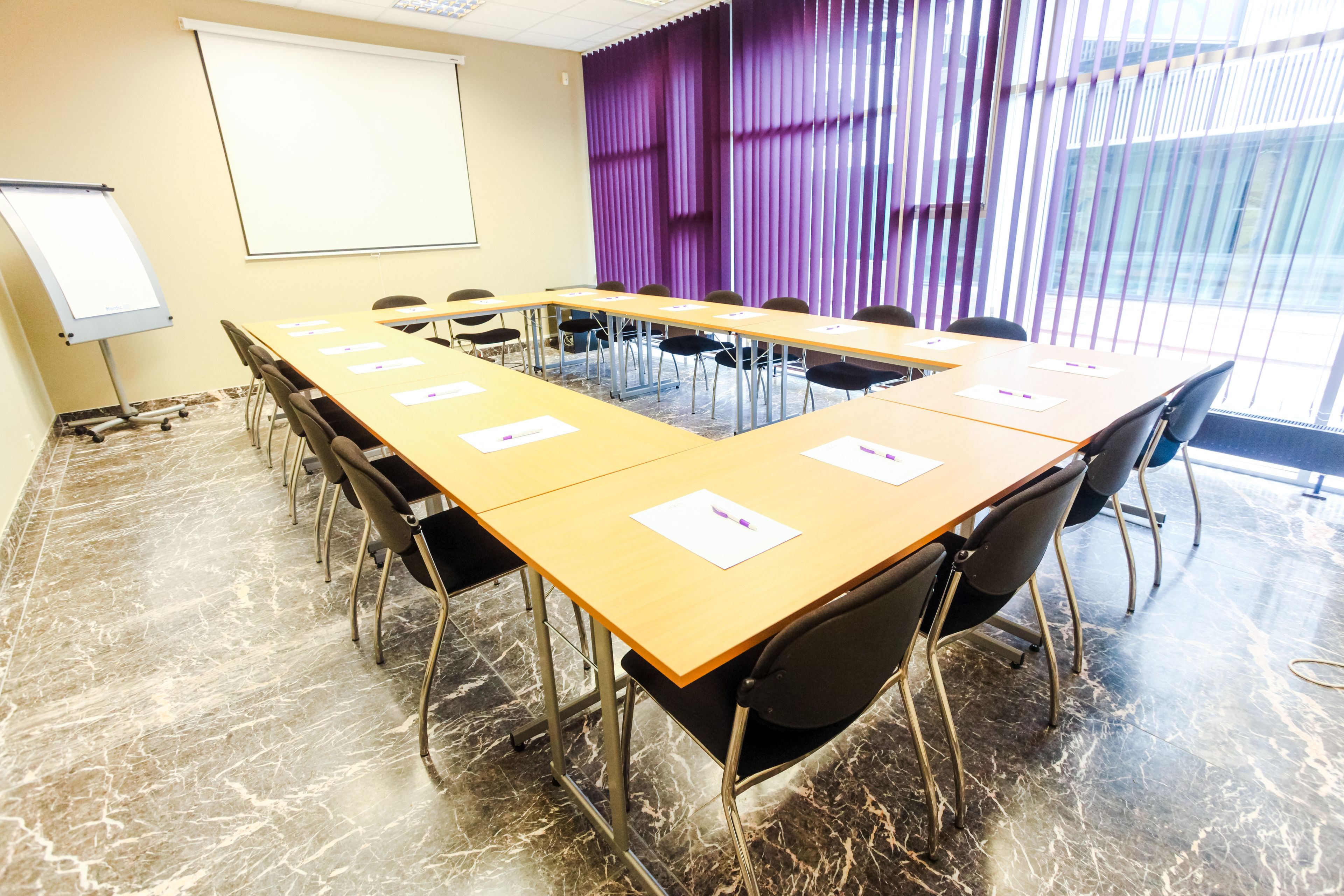 A conference room with a long table, chairs, a whiteboard, and a projector screen.
