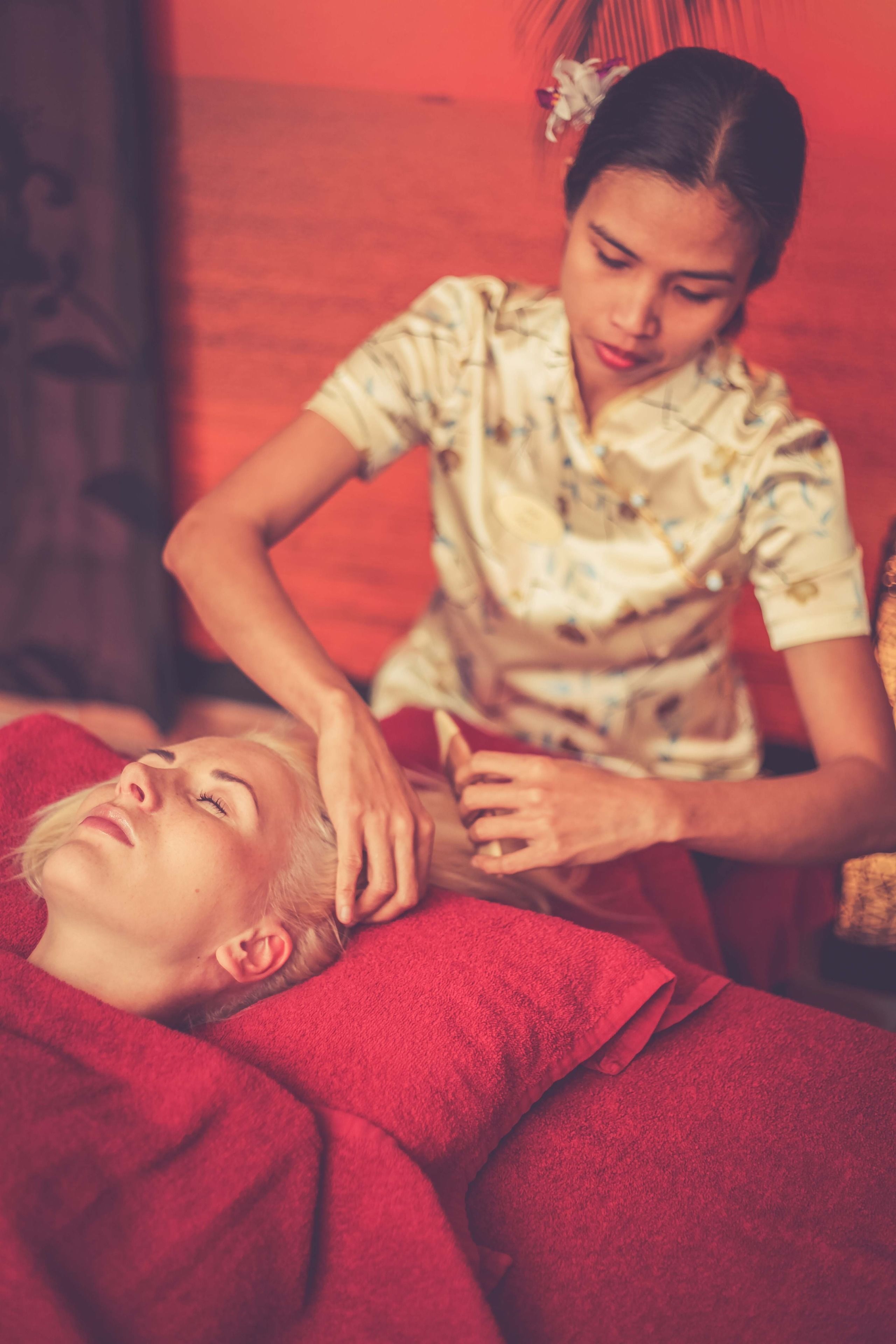 Uma pessoa recebendo massagem em um quarto com manta vermelha e cabeceira de madeira.