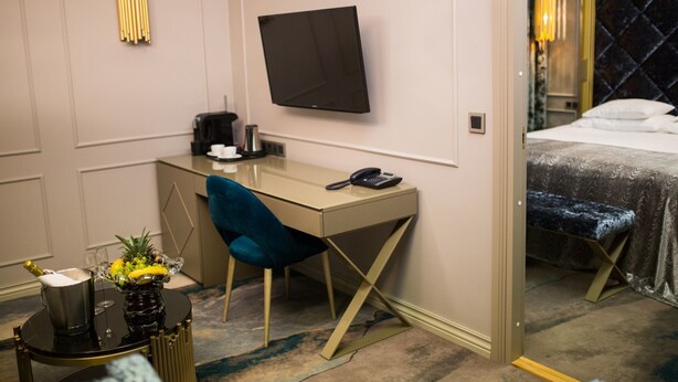A hotel room with a bed, a desk with a chair, a television, and a minibar.