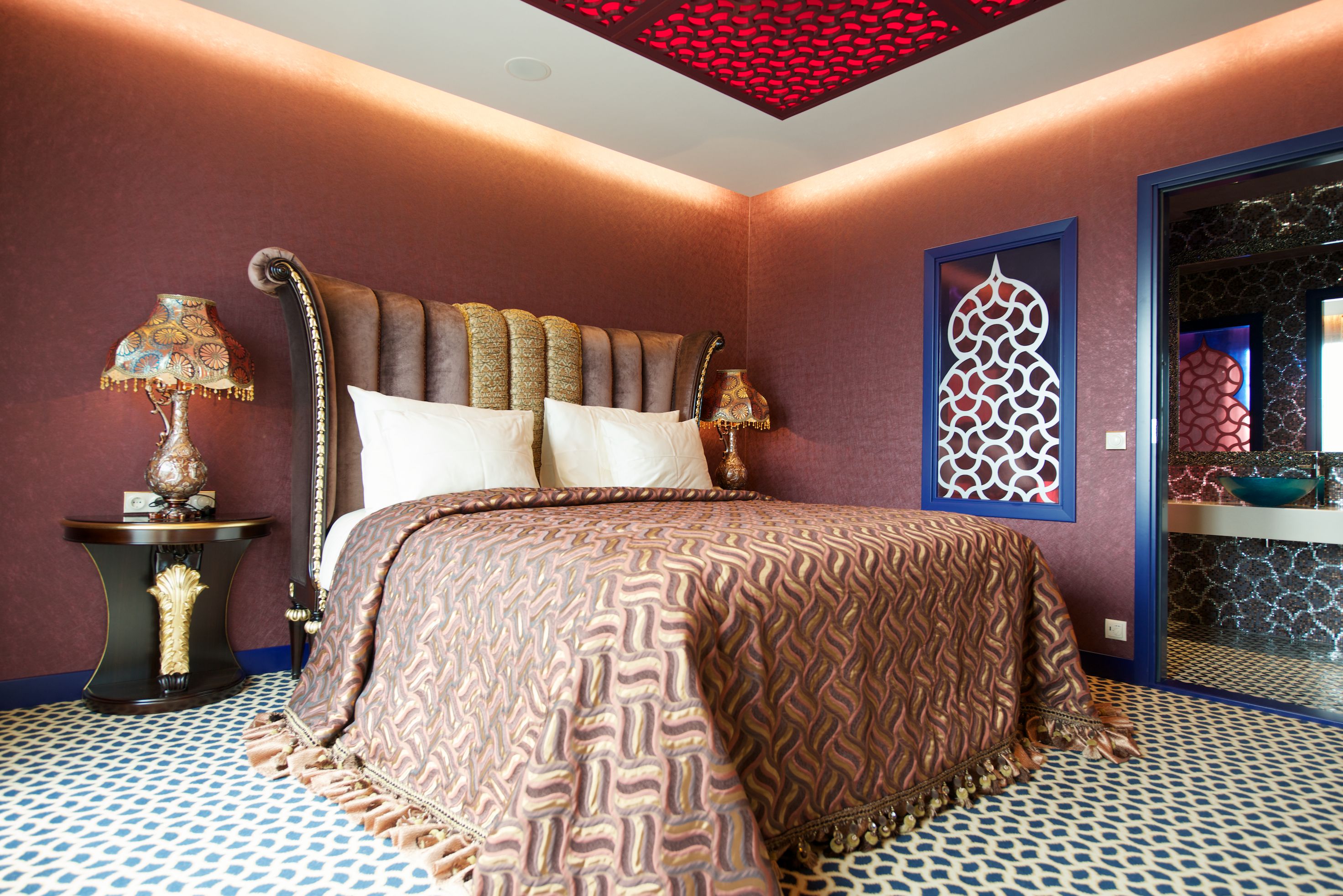 Un dormitorio con edredón estampado, dos lámparas de noche y un panel decorativo en la pared.