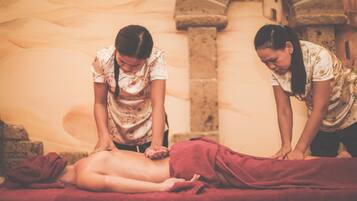 Eine Massageanwendung in einem Raum mit Steinwänden und einem roten Handtuch auf der Massageliege.