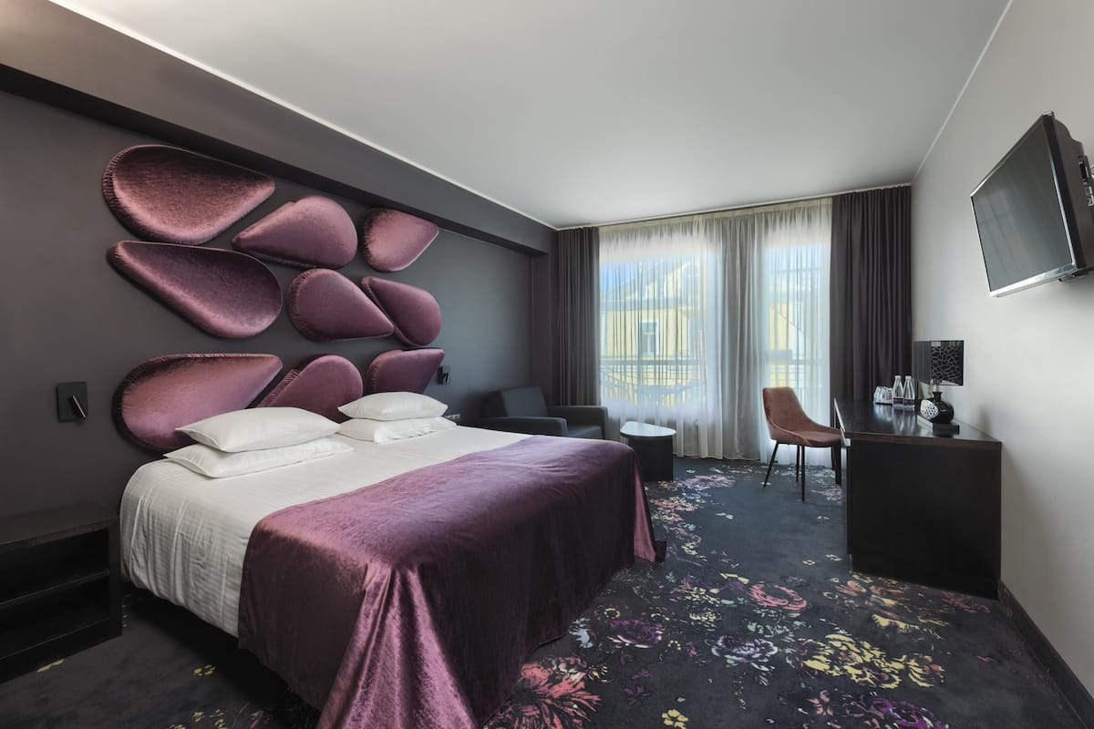 A modern hotel room with a large bed, a desk, and a TV.
