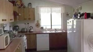 A compact kitchen with wooden cabinets, a microwave, a sink, and a refrigerator. - Staple House Bed and Breakfast (Woolooga)