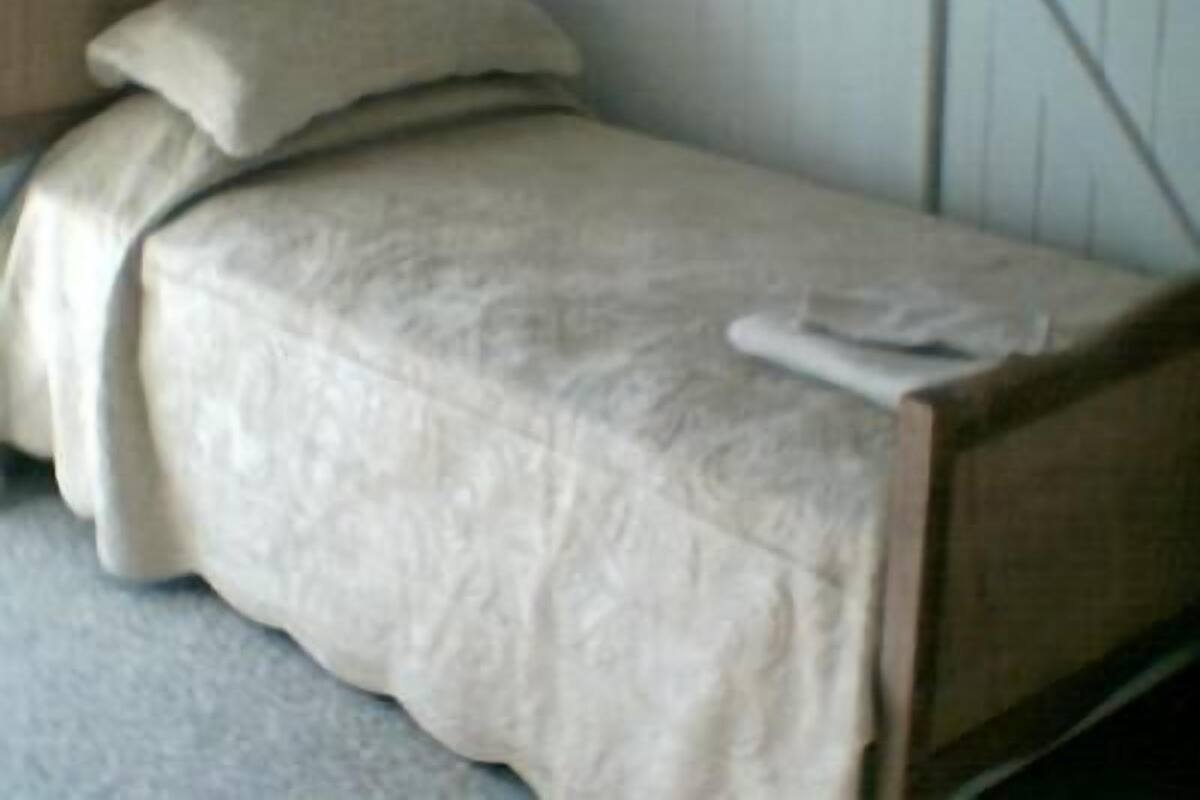 A small, single-bed room with a wooden headboard, a beige bedspread, and a single pillow.