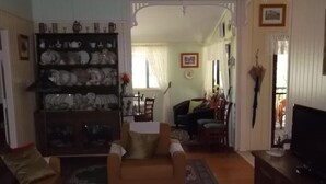 A living room with a brown sofa, a coffee table, and a bookshelf filled with decorative items. - Staple House Bed and Breakfast (Woolooga)