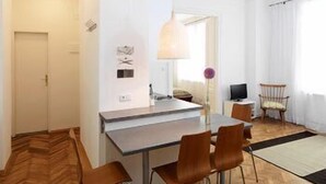 A compact living space with a kitchenette, a dining area with four chairs, a television, and a window with curtains.