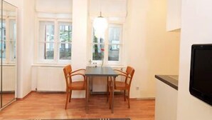 A compact room with a dining table and chairs, a small kitchen area, and a large window providing natural light.