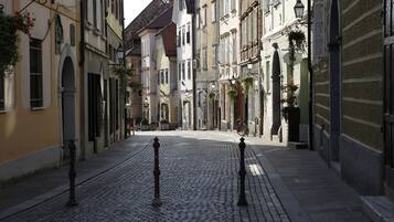A cobblestone street lined with historic buildings, featuring balconies with hanging plants and traditional street lamps.