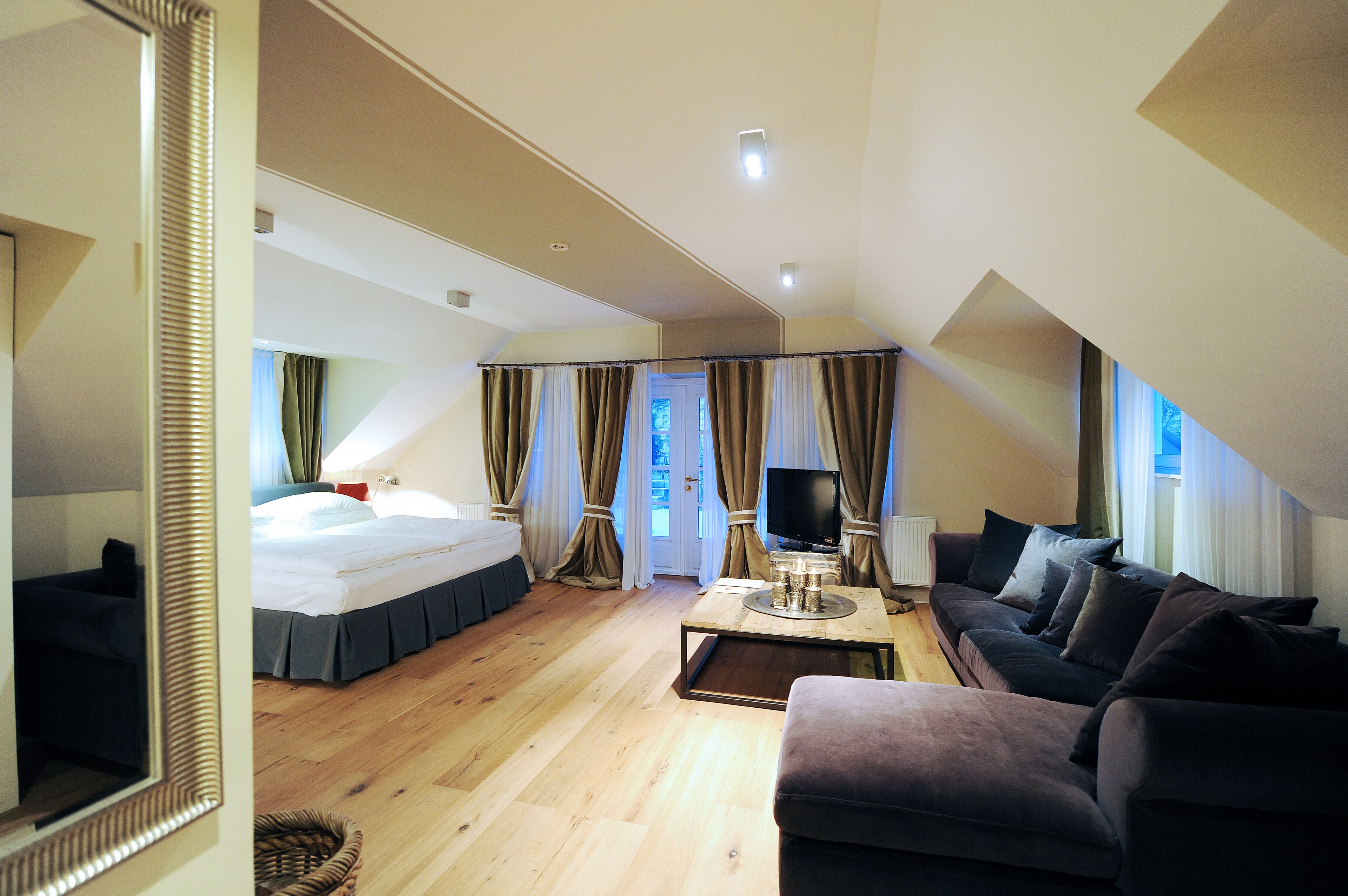 A modern hotel room with a bed, a sofa, a TV, and a dining table.