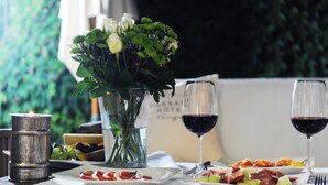 A dining table with a vase of flowers, two glasses of red wine, and plates of food. - Lesar Hotel Angel (Ljubljana)