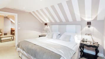 A bedroom with a large bed, two bedside tables with lamps, a wooden bench, and a door leading to another room.