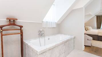 Une salle de bain moderne avec une baignoire sur pieds, un porte-vêtements en bois et un puits de lumière.