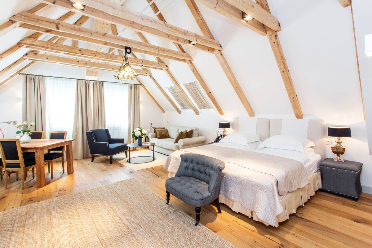A spacious loft bedroom with a high ceiling, wooden beams, a large bed, a desk, and a chair.