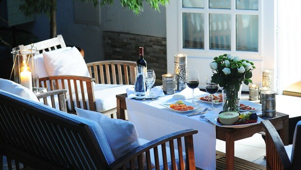 An outdoor dining area with a table set for two, surrounded by wooden chairs and a bench. - Lesar Hotel Angel (Ljubljana)