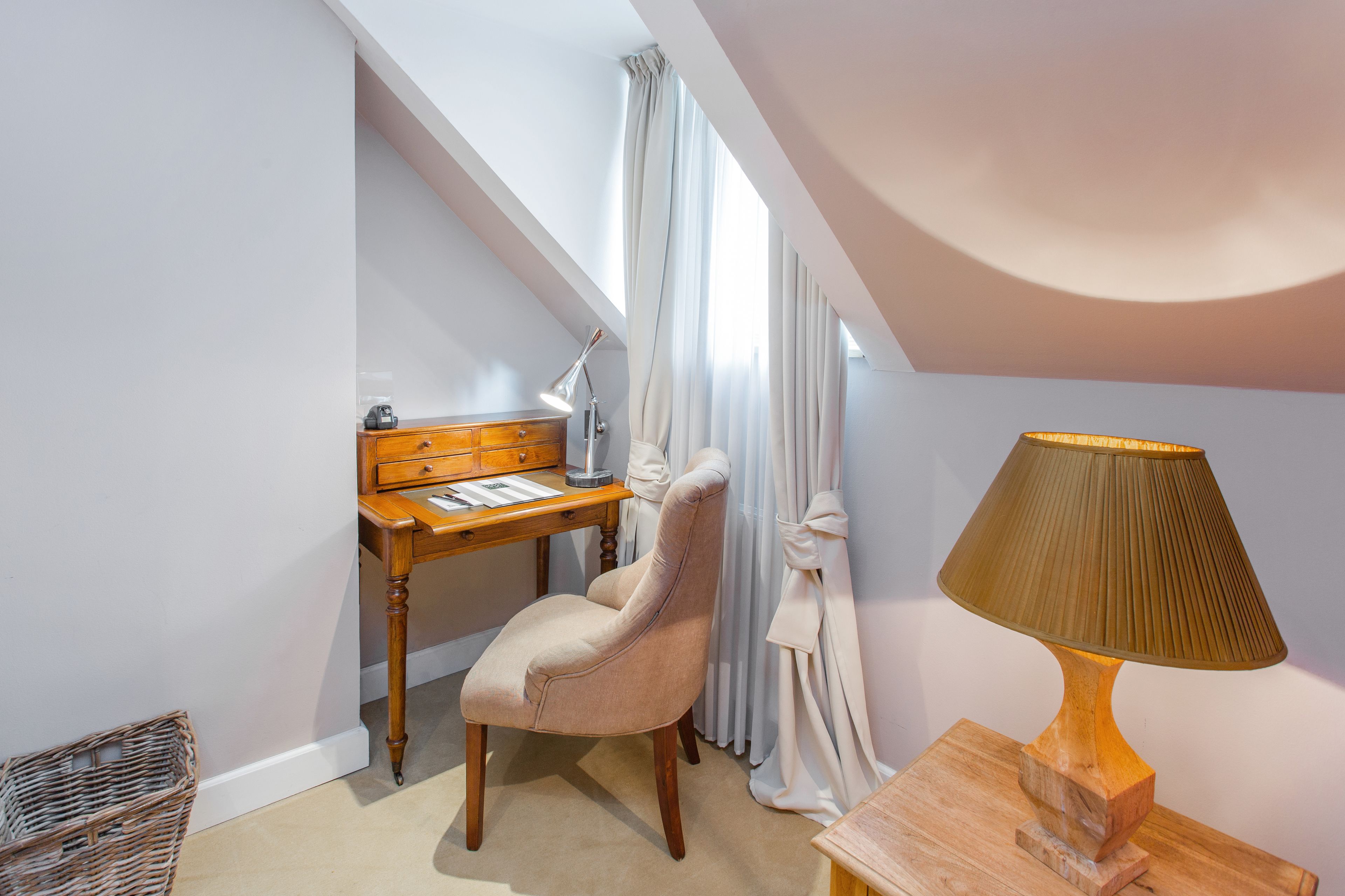 A room with a desk, chair, lamp, and a window with curtains.