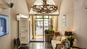 A hotel lobby with a reception desk, a sofa, a chair, a chandelier, and a view of the street outside. - Lesar Hotel Angel (Ljubljana)