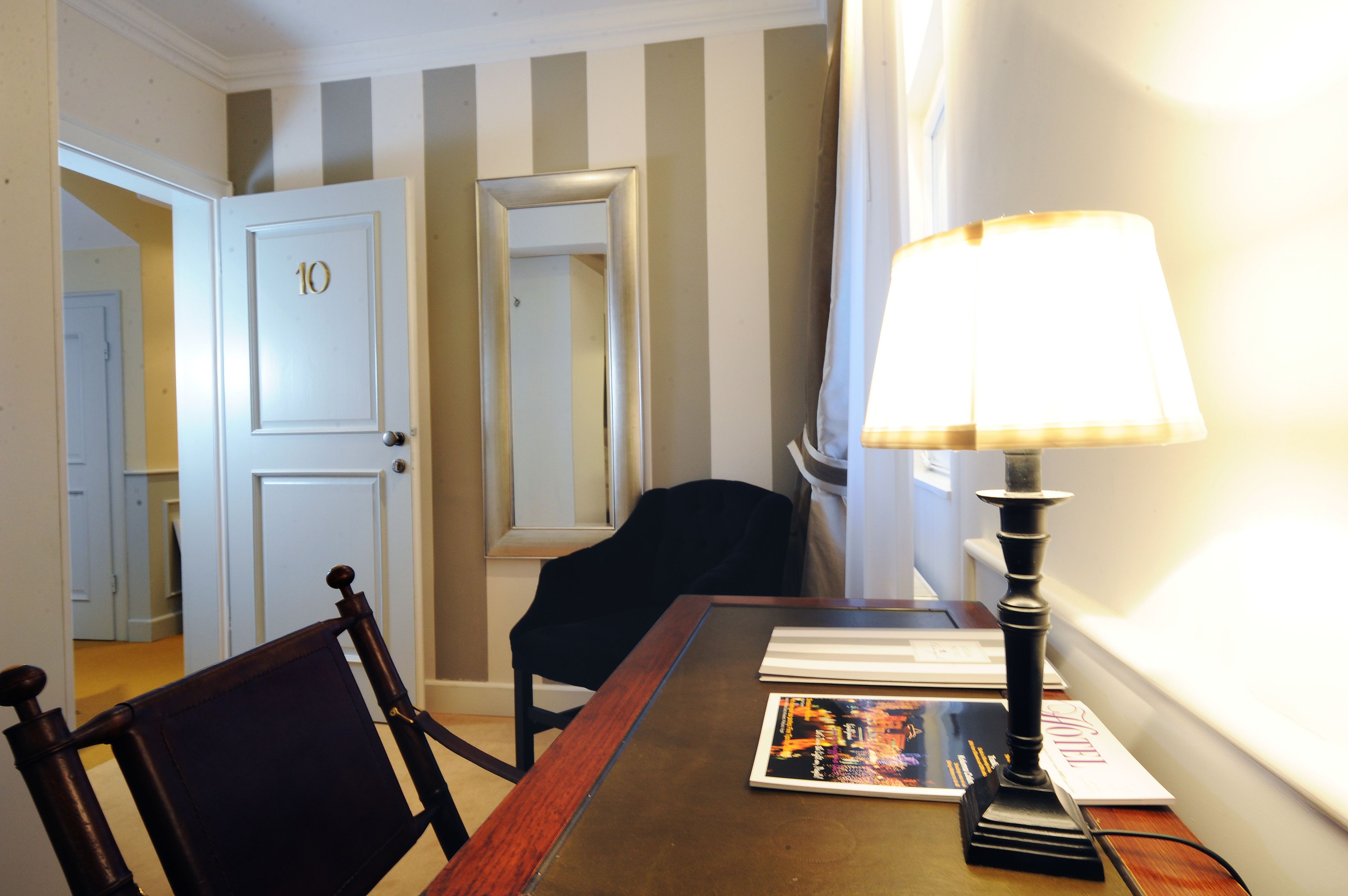 A hotel room with a wooden table, a black chair, a lamp, and a door with the number 10.