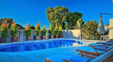 Una piscina al aire libre, sombrillas, sillones reclinables de piscina