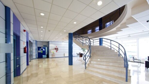 A spacious, modern lobby with a polished floor, a curved staircase, and a blue railing.